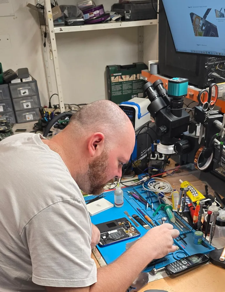 Technicien MICROTEK au travail sur un smartphone, sous microscope, sur un tapis antistatique entouré de ses outils